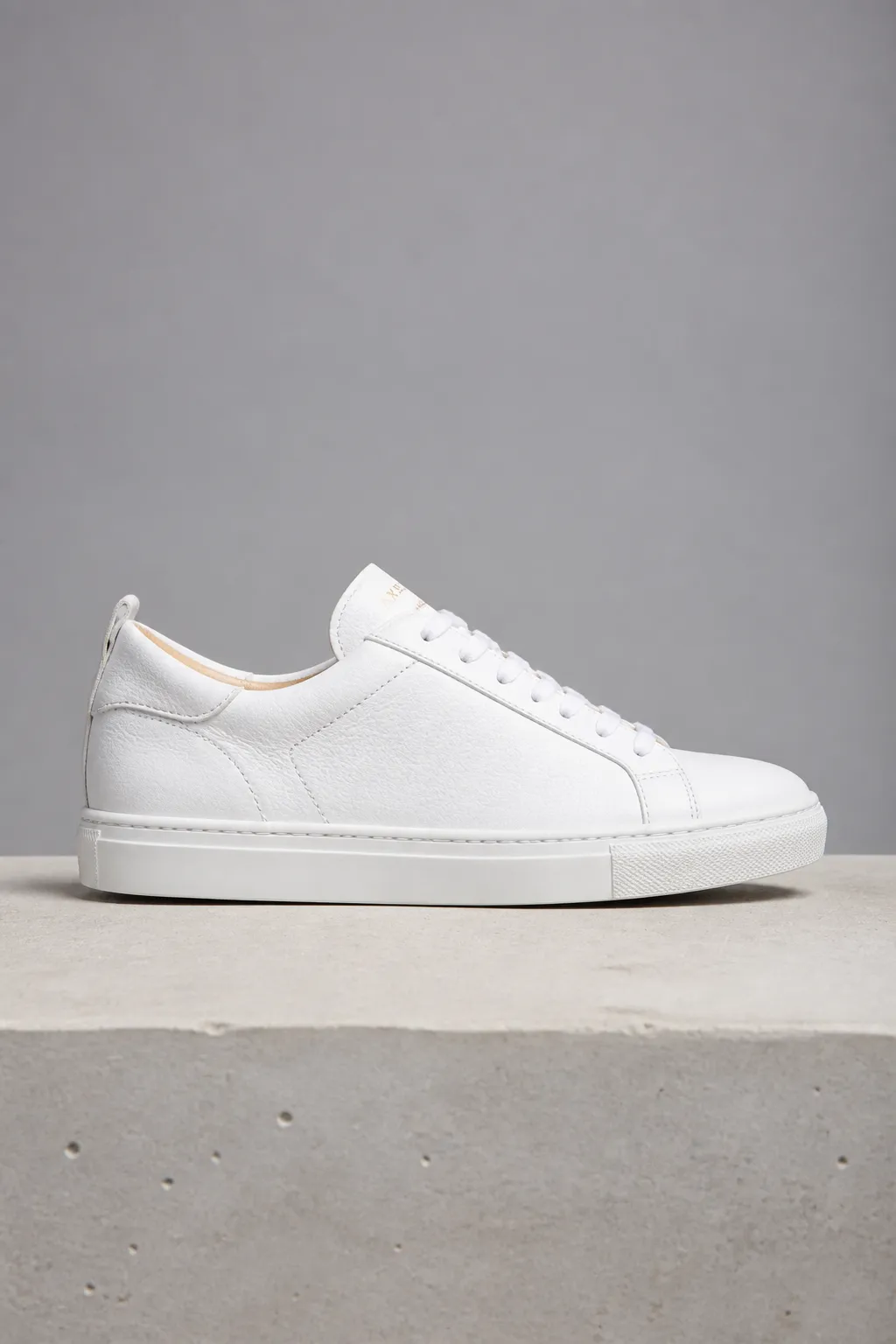 White leather low-top sneaker on a concrete block against a grey wall