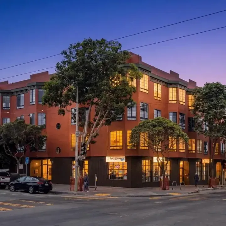 Dusk exterior of a four-story red brick apartment building on a city street corner